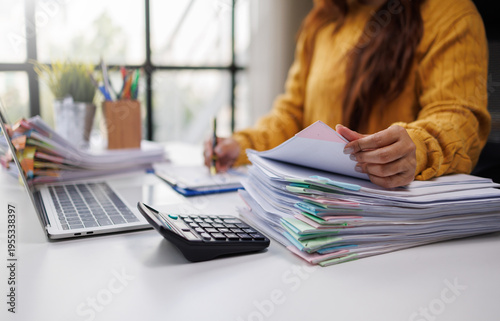Cuadro en lienzo A woman in a mustard sweater organizes colorful paperwork on her desk, while using a laptop, showcasing a busy and productive work environment with office supplies