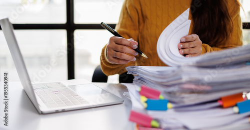 An individual engages in document review amidst stacks of papers, portraying real office dynamics and the complexities of managing numerous files and paperwork.