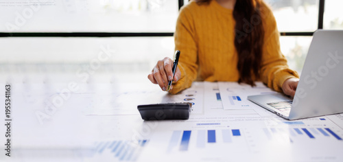 A dedicated individual is interacting with a calculator while analyzing reports and figures, illustrating the intensive nature of modern office tasks and data-driven decision-making.