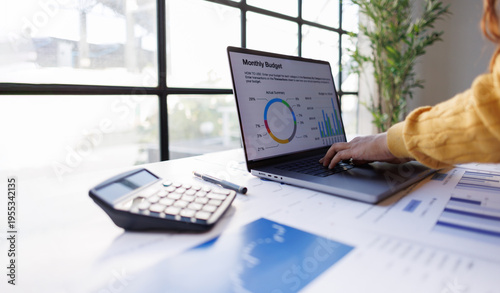 An insightful view of a laptop screen displaying a monthly budget overview accompanied by colorful graphs that illustrate spending patterns and financial insights within an organized space.