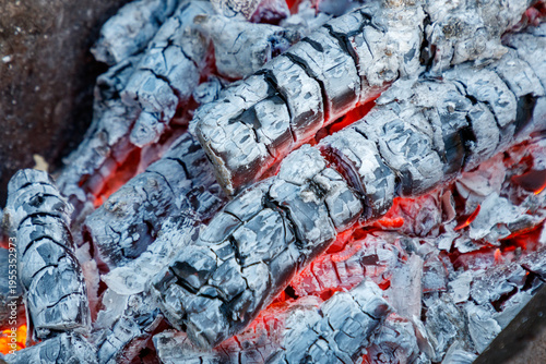 Charcoal briquettes burn with visible red-hot embers and ash