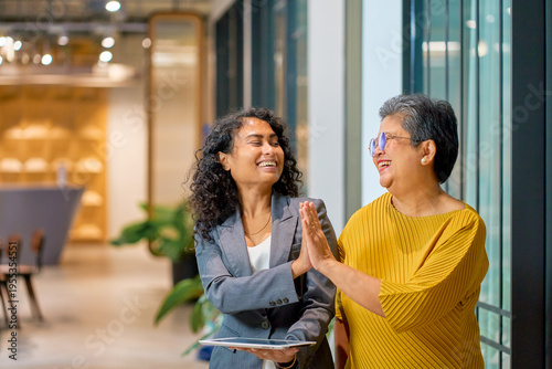 Happy and smilely scene of senior advisor and young besinesswoman touch hand for celebrate in work place.