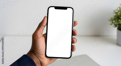 Close up hand holding modern smartphone with white blank screen in minimal home office