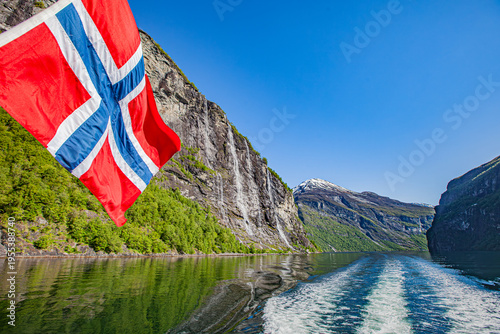 Bandera Noruega ondeando con la cascada de las siete hermanas de fondo navegando por el fiordo Geiranger.