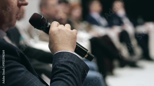 Man speaking into microphone at business conference panel discussion, audience participation and professional communication at corporate event indoors.