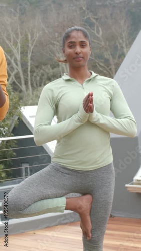 Vertical video: Starting rooftop yoga Indian yogi holding tree pose on deck, green top, centering