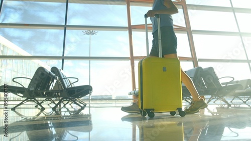 Quadro em tela Traveler pulling yellow luggage through a modern airport departure lounge, embar