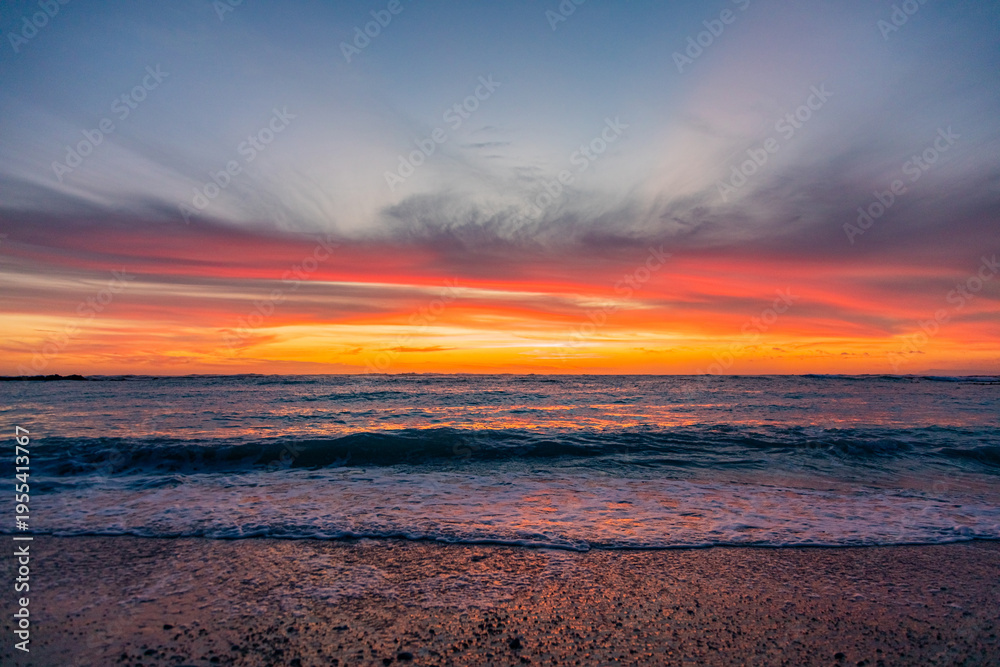 Fototapeta premium Dramatic Golden sunset over tranquil beach, waves lashing the pebble coastline