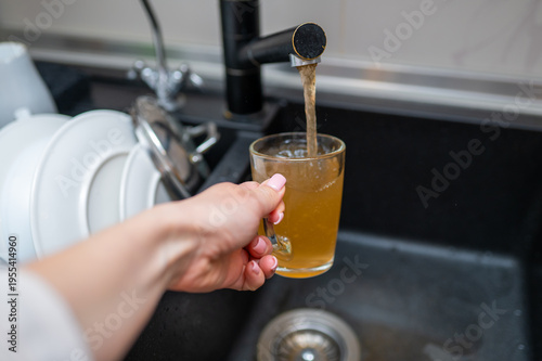 Hand Holding Glass Mug Filling with Dirty Rusty Water from Kitchen Faucet Poor Tap Water Quality