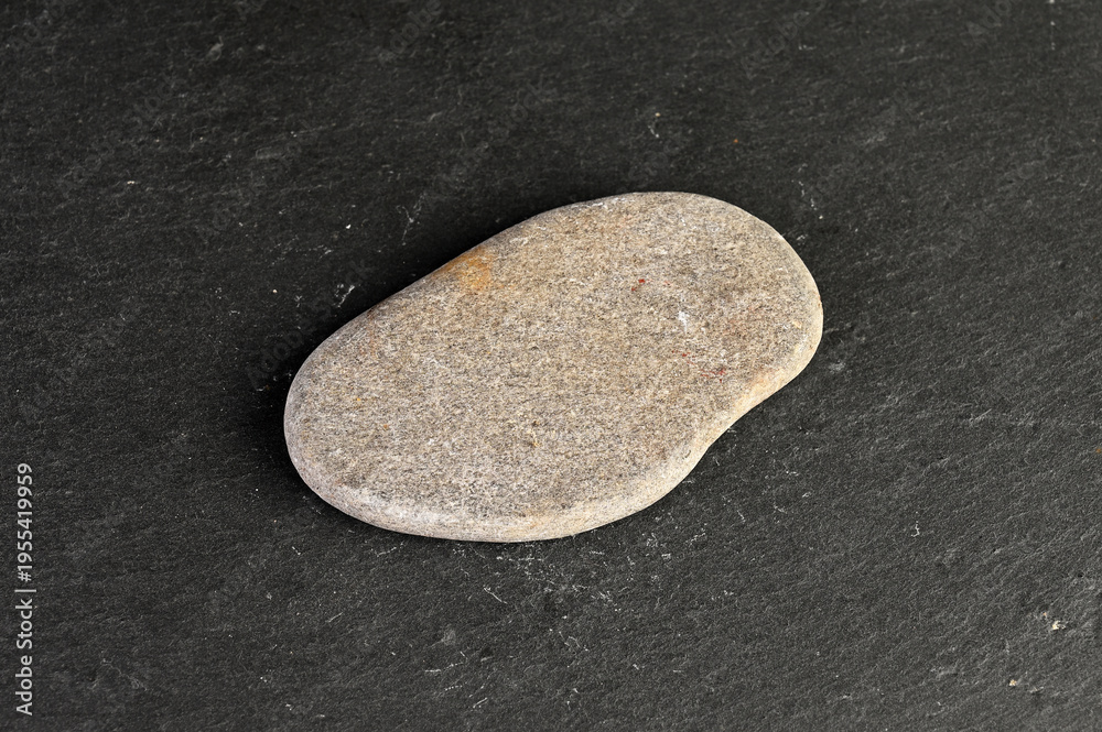 Obraz premium Smooth, rounded pebble resting on a dark, textured stone surface