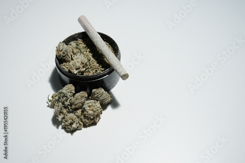 Marijuana joint on top of a black grinder with buds isolated on white