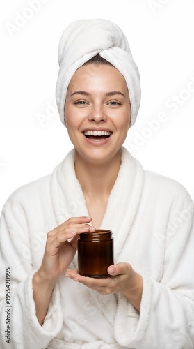 Laughing woman in white bathrobe and towel holding an amber glass cosmetic jar on white background
