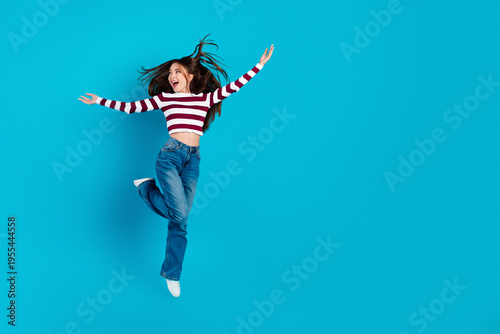 Fotografie Happy young woman jumping with joy on a bright blue background wearing striped s