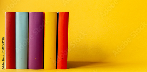 Five books with small roman numerals on their spines on a yellow background with space for additional content.