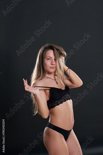 Black lingerie set with lace inserts. A girl poses in a studio. Long hair flows down her back. Concept for fashion campaigns. Demonstration of modern fashion.