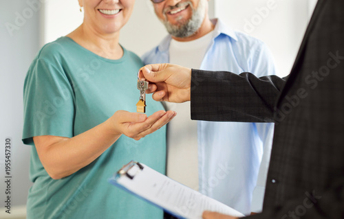 Fotografija Realtor agent giving house key to a smiling mature senior couple during closing, symbolizing their ownership and completion of purchase as documents are signed