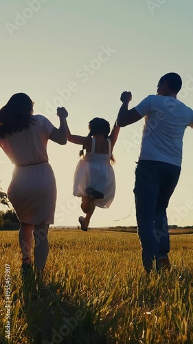 A woman and a man joyfully lift a girl in the air against a bright sunset. The scene captures a moment of happiness in a sunny field filled with tall grass.