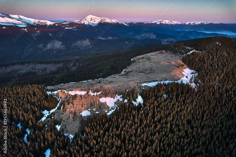Fototapeta premium Beautiful landscape of spruce trees, deforested hill and snow-caped mountains under evening sky