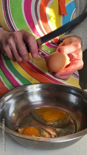 Cracking eggs into an empty metal bowl for dough preparation, vertical video, side view
