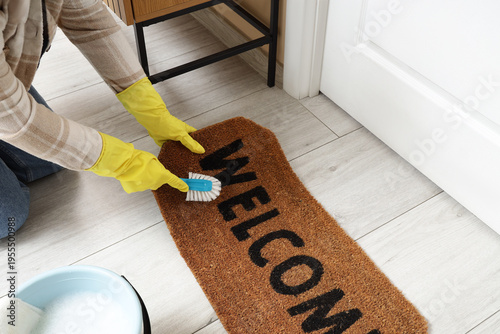 Canvas-taulu Woman cleaning doormat with brush in hallway