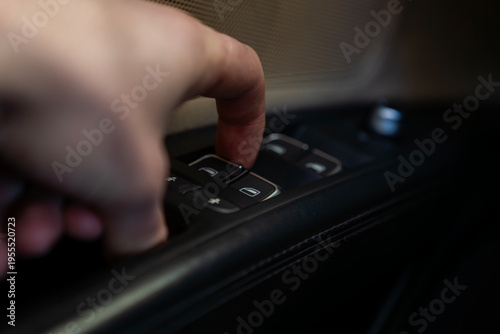 Hand pressing power window switch on car door panel, close up of control buttons and speaker grille, automotive interior detail.