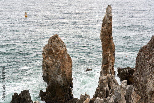 A high-angle view captures the iconic Chuam Candlestick Rock and surrounding sea stacks at Sol Beach, Samcheok, South Korea, with white surf crashing against the base under a cloudy sky.