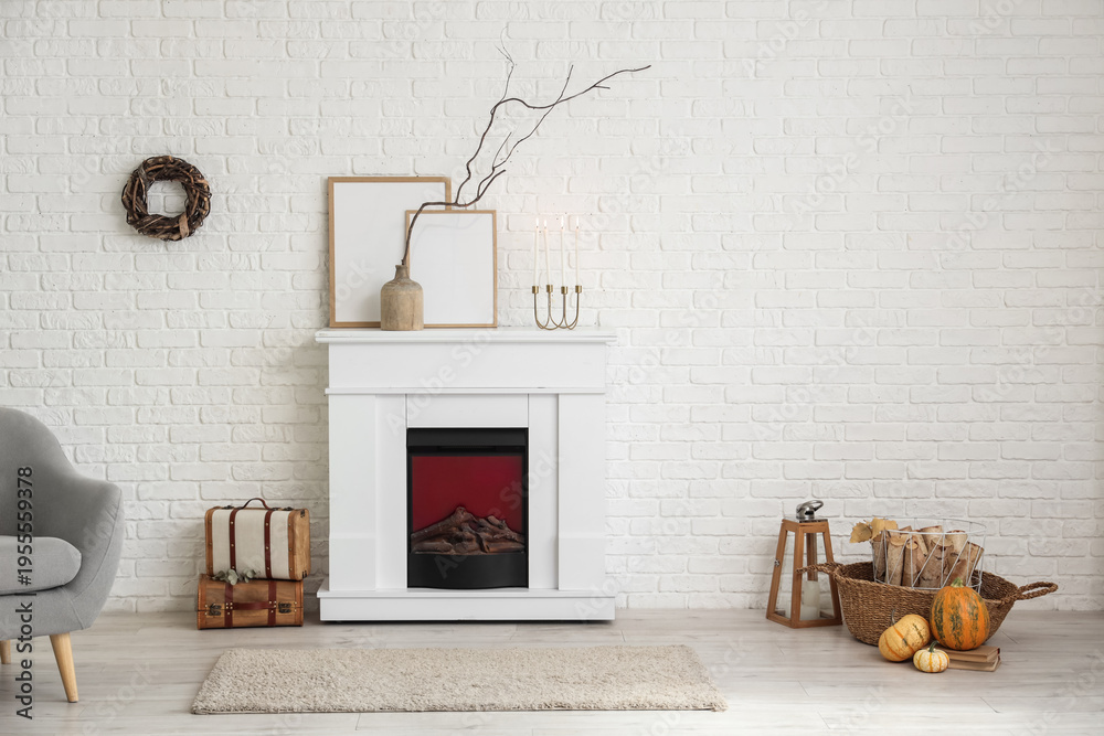 Naklejka premium Interior of stylish room with modern fireplace, armchair and autumn decorations near white brick wall