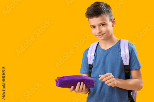 Little schoolboy with pencil case on orange background