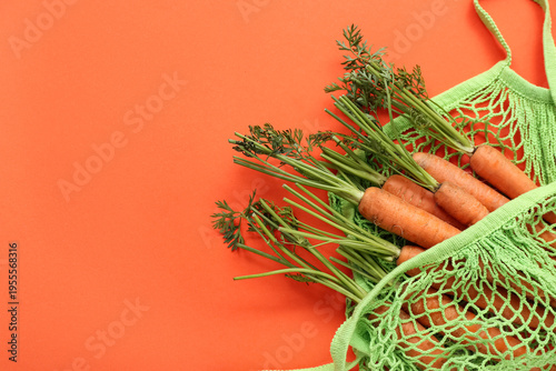 String bag with fresh carrots on orange background