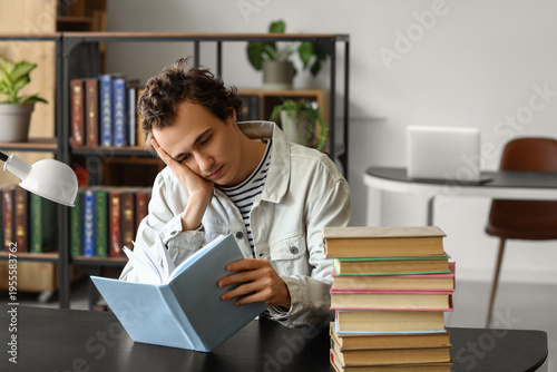 Tired young man reading boo...