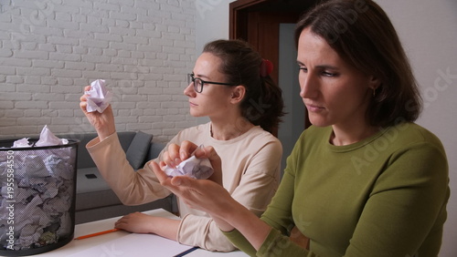 Schilderij op canvas Two women are sitting at a desk, looking frustrated and stressed while crumpling