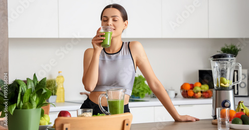 Sporty young woman drinking healthy smoothie in kitchen