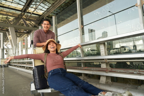 An Asian couple, a man and his girlfriend, were walking in front of the airport terminal after arriving for a trip and were looking for a rental car to travel to their destination.