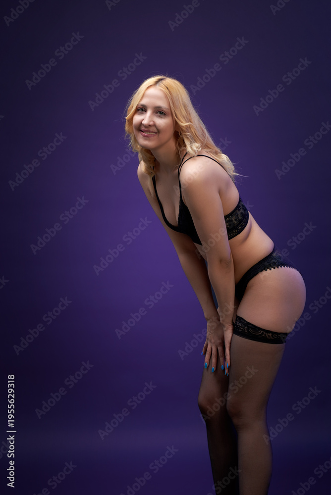 Fototapeta premium A woman with a beautiful figure in black lingerie poses against a dark background.
