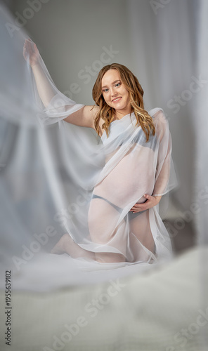 The happy expectant mother kneeling on the bed and smiling.