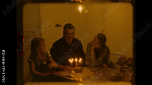A family is gathered around a table with a lit birthday cake in a cozy room at night on analog super 8 film