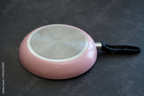 Pink frying pan upside down on dark surface. Pink frying pan placed upside down on a dark surface, showing the metallic textured bottom.