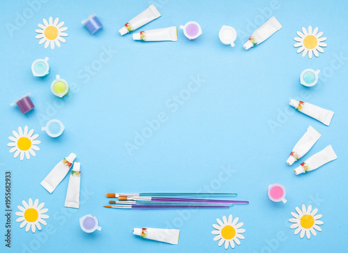 Paintbrushes with colorful paints and spring flowers on blue background. Creativity, artistic inspiration, celebration of World Art Day