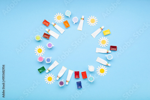 World Art Day background with paintbrushes, colorful paints and spring flowers on blue, copy space for poster, art class, kids workshop or social media design