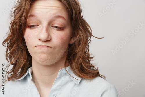 Bild auf Leinwand Young woman with wavy hair looks down with a doubtful expression wearing a light shirt