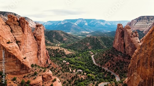 Scenic desert canyon road winds through lush green valley with towering red rock formations