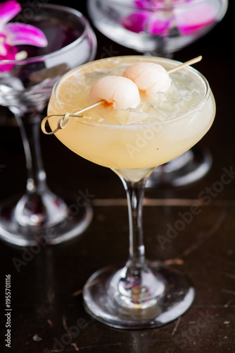Lychee martini served in an elegant glass, featuring a crystal-clear, chilled cocktail infused with delicate lychee flavor. Garnished with whole lychees and edible flowers, 