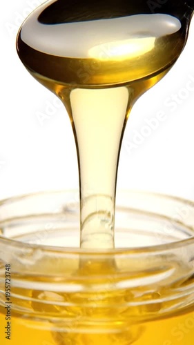 Golden honey pouring from spoon into a jar on white background, perfect for food or health-related uses