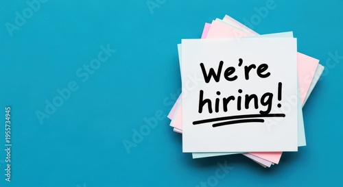 We're Hiring! handwritten text on white sticky notes stack on a vibrant blue background, recruitment concept