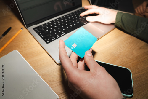 A person uses a credit card to make an online purchase on a laptop, with a smartphone nearby.