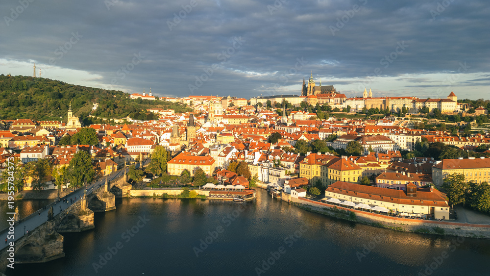 Obraz premium The early morning light casts a warm glow over the historic Charles Bridge and the majestic Prague Castle. The Vltava River reflects the stunning architecture of the city, creating a beautiful scene.