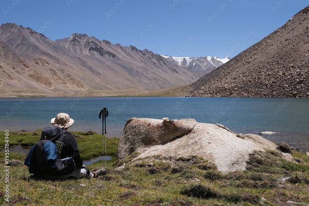 Fototapeta premium Amazing scenery of turquoise Guharrez (Zaroshkul) Lake and silhouette of sitting trekker in Pamir Mountains,Tajik National Park, Gorno - Badakhshan, Tajikistan