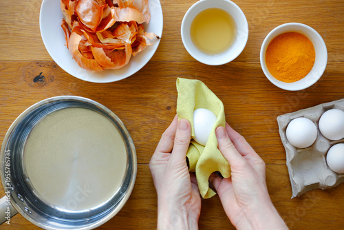 Natural easter egg preparation with onion skins and turmeric, female hands cleaning white egg before dyeing, eco friendly traditional method, rustic kitchen scene with copy space
