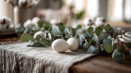 Linen table runner on a farm table decorated with eucalyptus branches and white ceramic eggs. Homey atmosphere, soft neutral colors, sharp focus on foreground, blurred background.