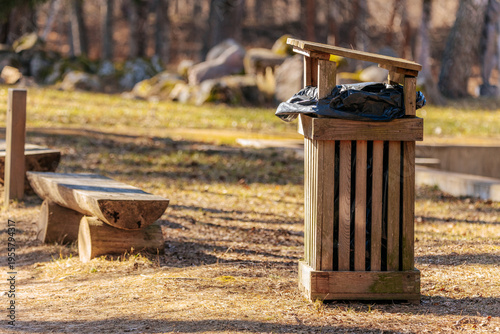 Foto Wooden trash bin with black garbage bag in a park setting, surrounded by grass a
